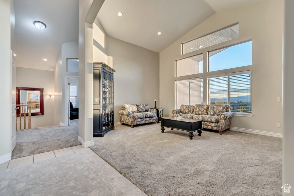 Living room with light colored carpet, high vaulted ceiling, healthy amount of natural light, light tile patterned flooring, and baseboards