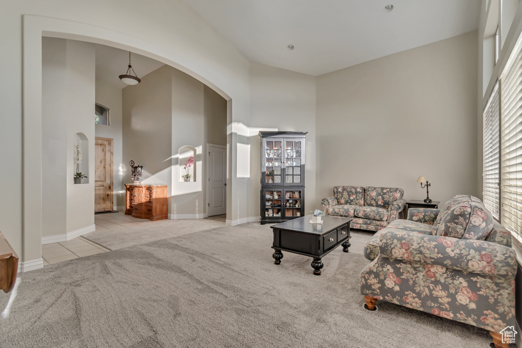 Carpeted living room with arched walkways, a high ceiling, baseboards, and tile patterned flooring