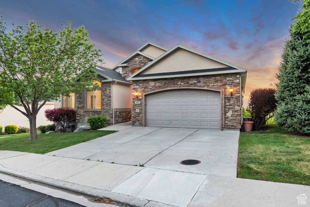 View of front of home with stone siding, driveway, a front yard, stucco siding, and an attached garage