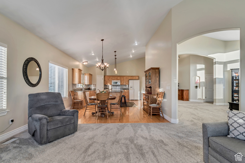Living room featuring light carpet, a chandelier, arched walkways, healthy amount of natural light, and high vaulted ceiling