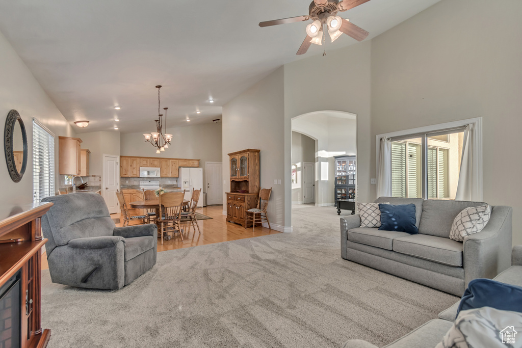 Living area with light carpet, arched walkways, ceiling fan, high vaulted ceiling, and a chandelier