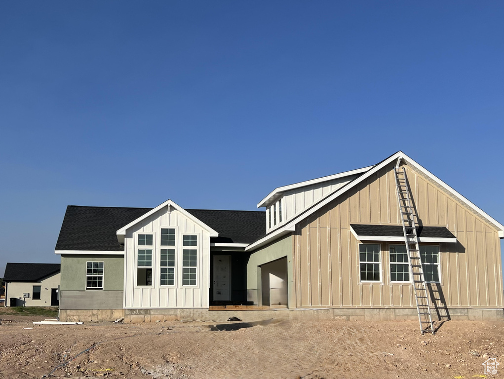 View of front of house with board and batten siding, an attached garage, and roof with shingles