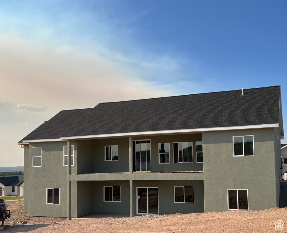Rear view of property featuring stucco siding, a shingled roof, and a patio