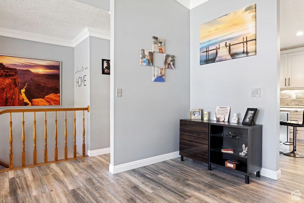 Corridor featuring wood finished floors, baseboards, crown molding, a textured ceiling, and recessed lighting