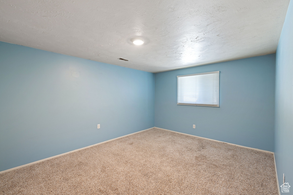 Carpeted empty room featuring a textured ceiling and baseboards