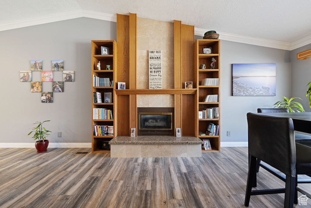 Living area featuring a fireplace, wood finished floors, baseboards, lofted ceiling, and ornamental molding