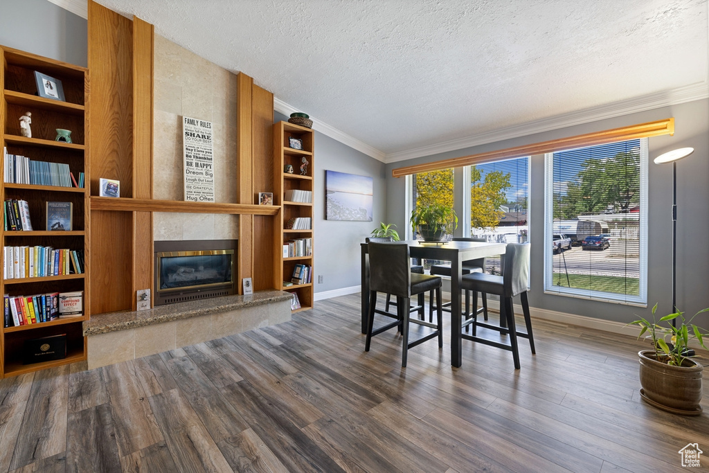 Dining space featuring a textured ceiling, a tile fireplace, baseboards, ornamental molding, and wood finished floors