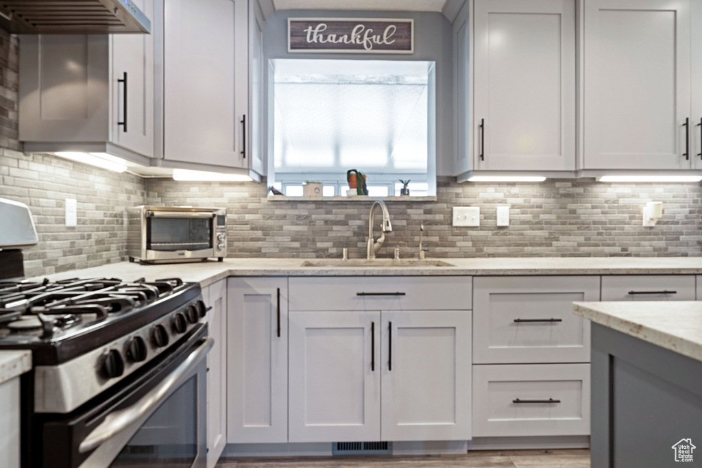 Kitchen with gas range, a sink, tasteful backsplash, light stone countertops, and under cabinet range hood