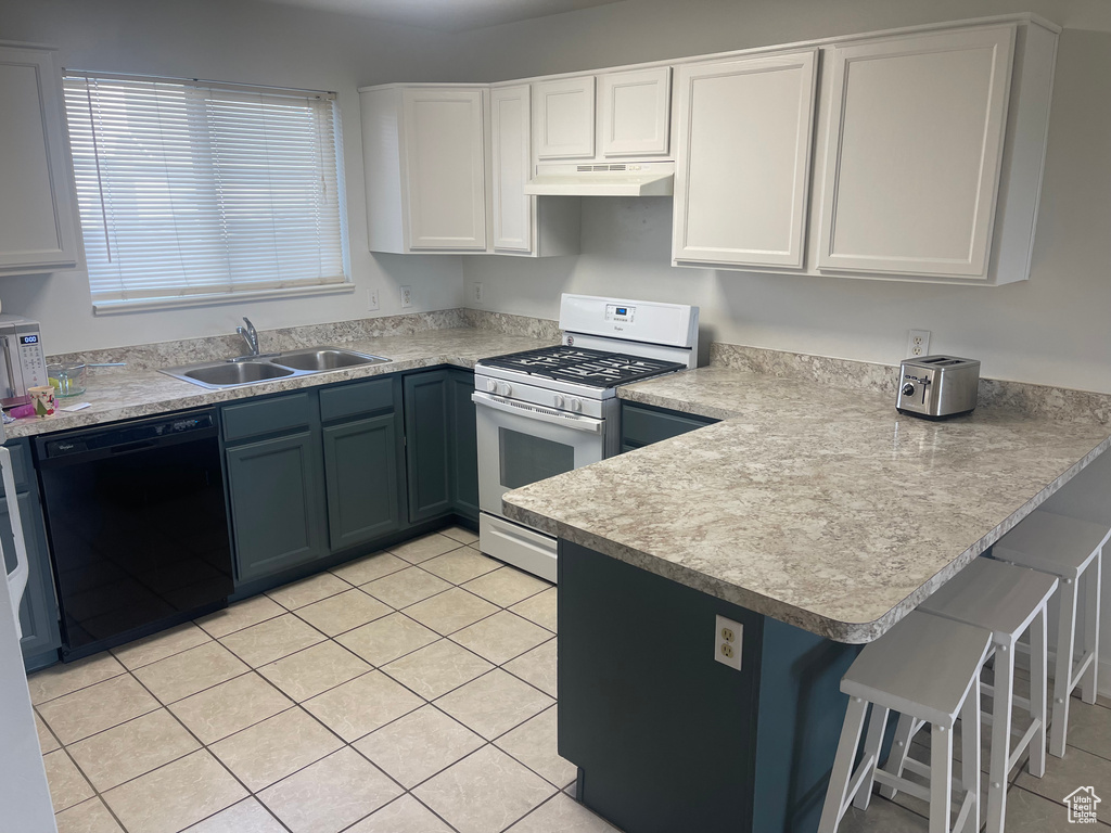 Kitchen featuring black dishwasher, white gas range oven, under cabinet range hood, a sink, and a peninsula