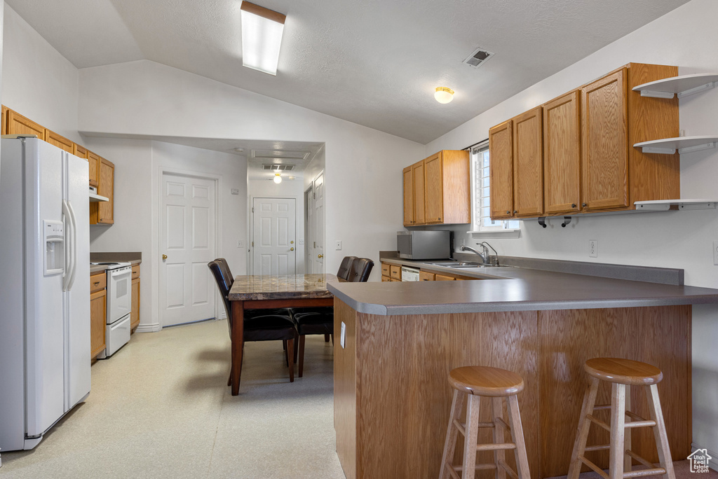 Kitchen featuring white appliances, open shelves, vaulted ceiling, a peninsula, and a sink