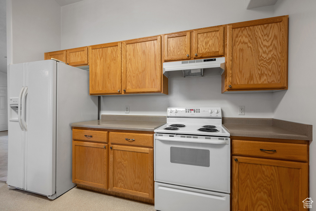 Kitchen with white appliances, under cabinet range hood, and brown cabinetry