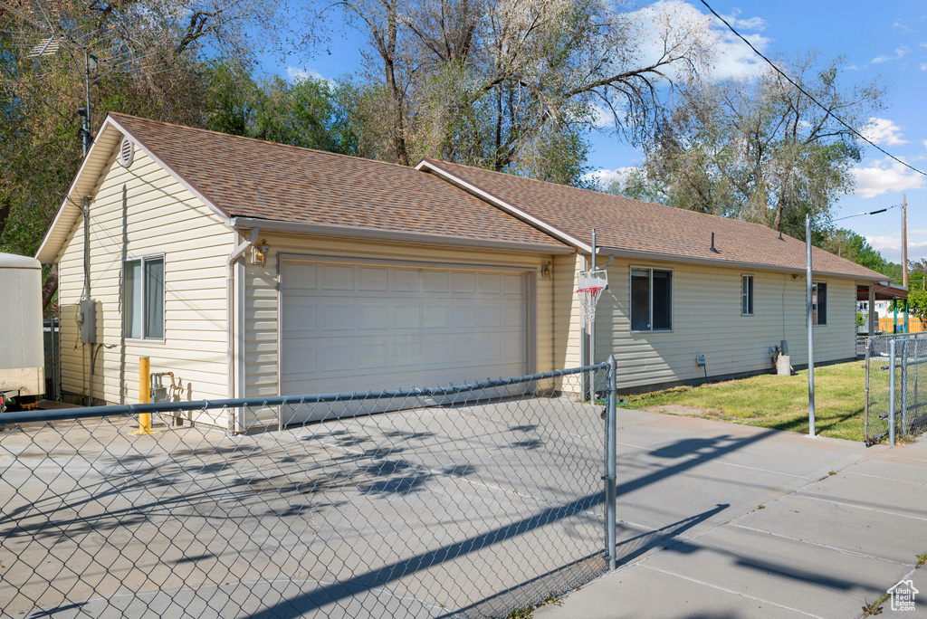 Ranch-style house featuring fence, concrete driveway, a shingled roof, and an attached garage