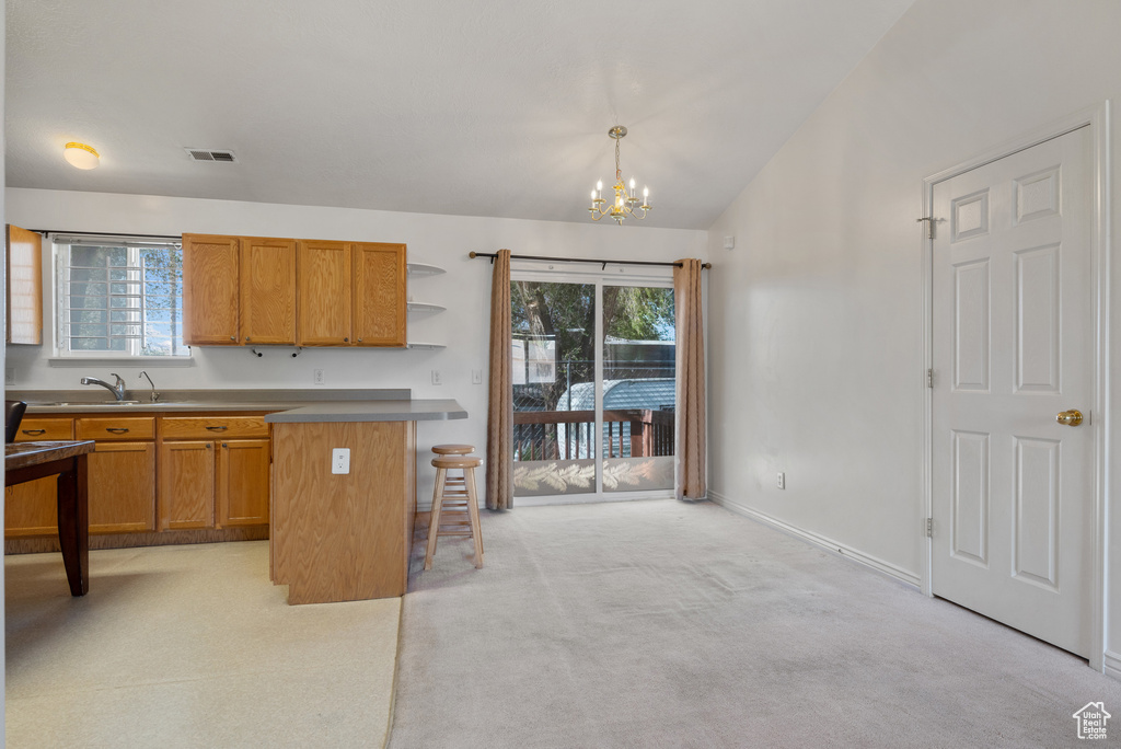 Kitchen with a kitchen bar, open shelves, a chandelier, light carpet, and brown cabinets