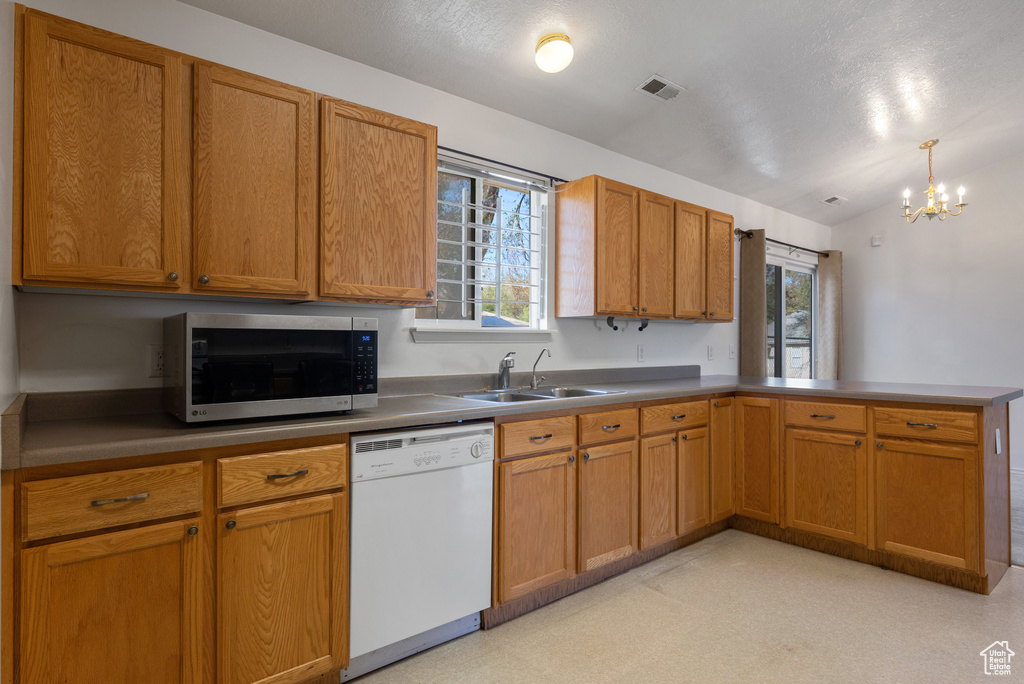 Kitchen featuring white dishwasher, stainless steel microwave, a sink, a peninsula, and a chandelier