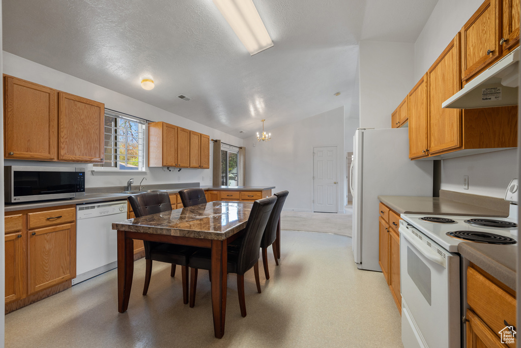 Kitchen with white appliances, a chandelier, lofted ceiling, a peninsula, and under cabinet range hood