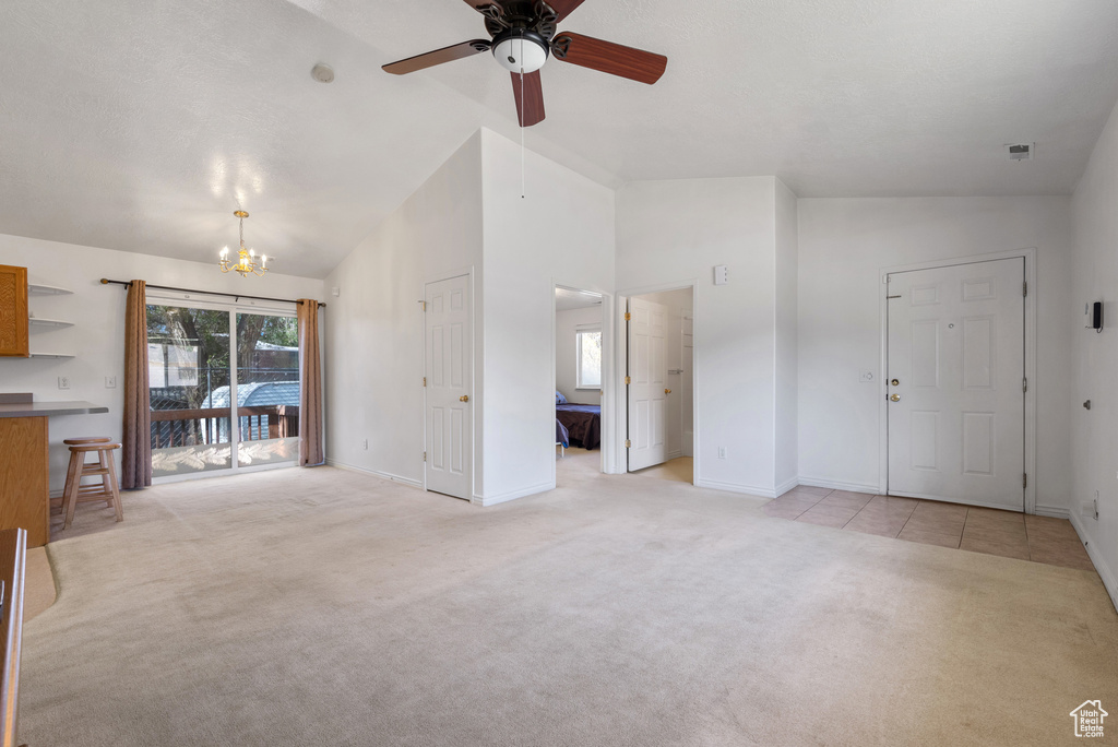 Unfurnished living room featuring light carpet, baseboards, a chandelier, ceiling fan, and high vaulted ceiling
