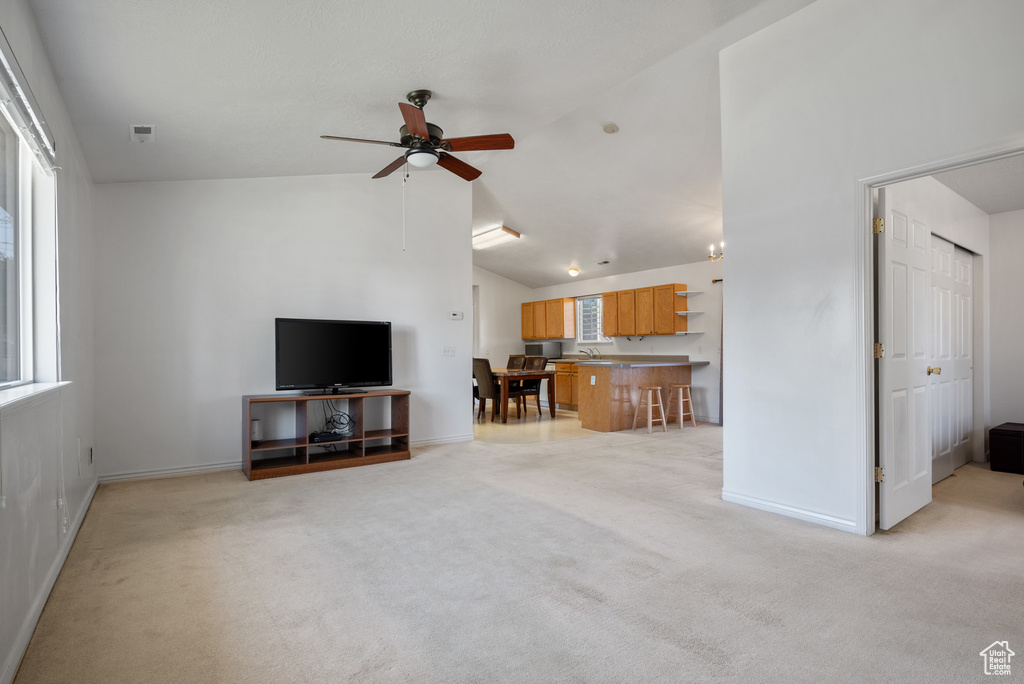 Living area with ceiling fan, light carpet, baseboards, and high vaulted ceiling