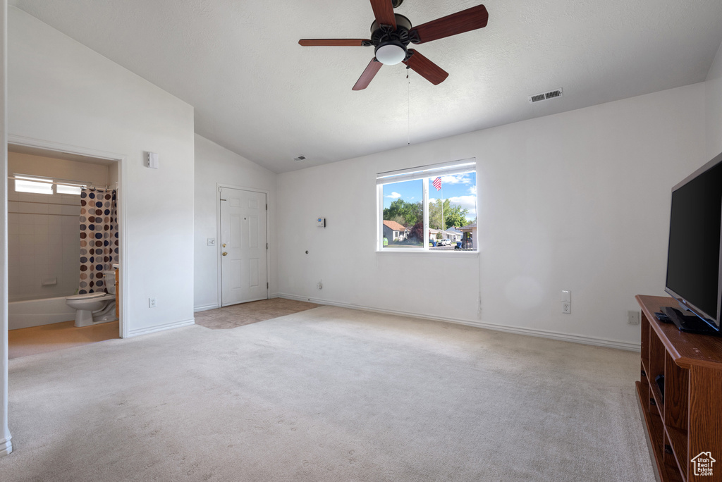 Unfurnished living room featuring light carpet, vaulted ceiling, a ceiling fan, plenty of natural light, and baseboards
