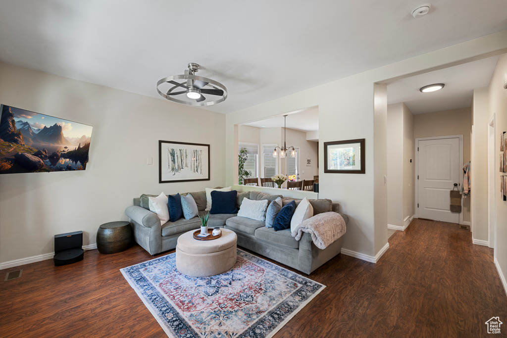 Living room with ceiling fan with notable chandelier, baseboards, visible vents, and wood finished floors