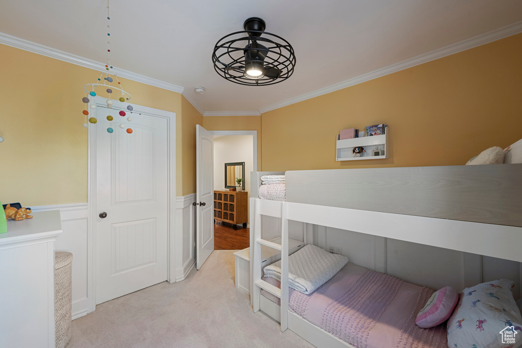 Bedroom with crown molding, light carpet, a wainscoted wall, and a closet