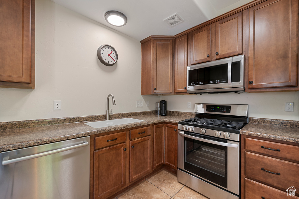 Kitchen with light tile patterned floors, visible vents, a sink, dark countertops, and stainless steel appliances