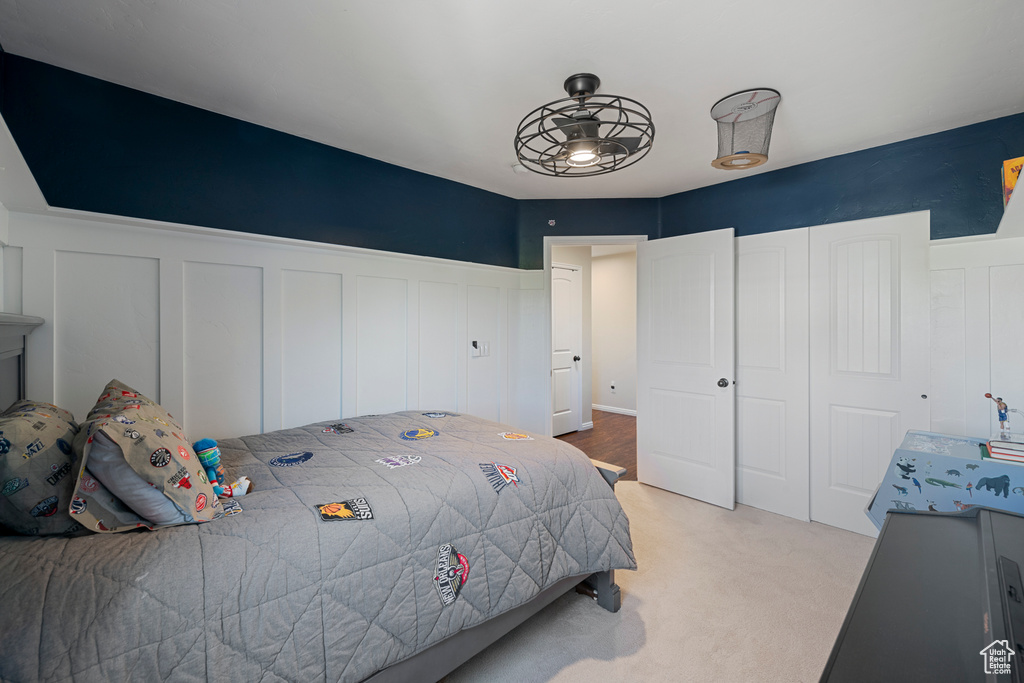 Bedroom featuring light colored carpet, a closet, a decorative wall, and wainscoting