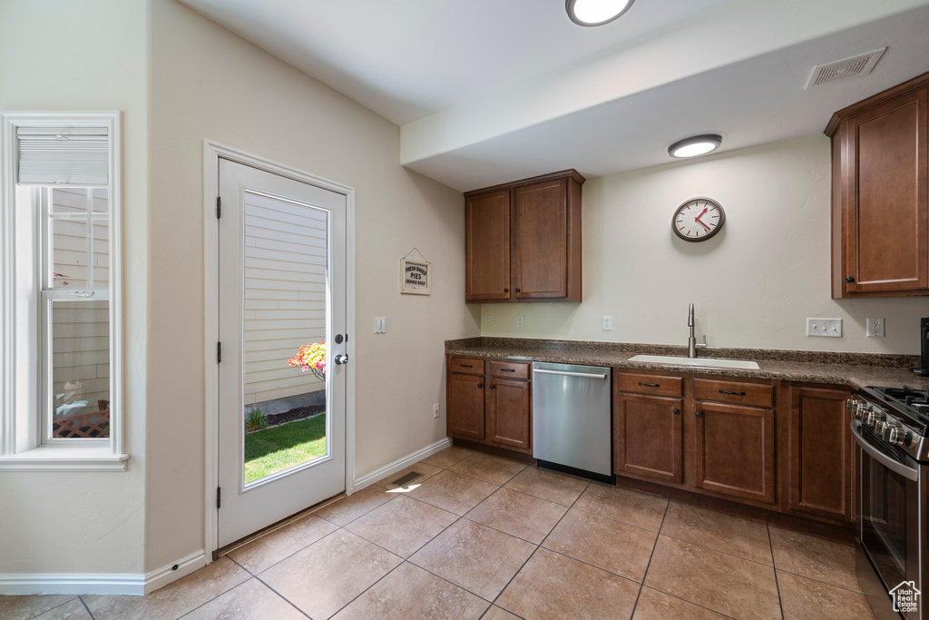 Kitchen with light tile patterned floors, a sink, dark countertops, stainless steel appliances, and visible vents