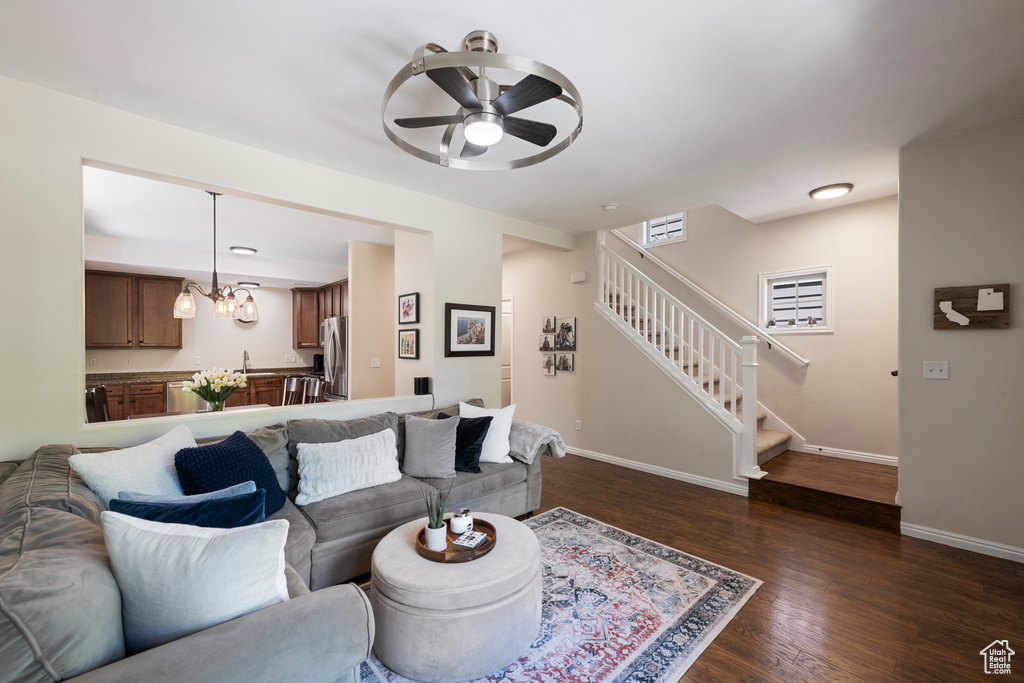 Living room with stairway, ceiling fan with notable chandelier, baseboards, and dark wood finished floors