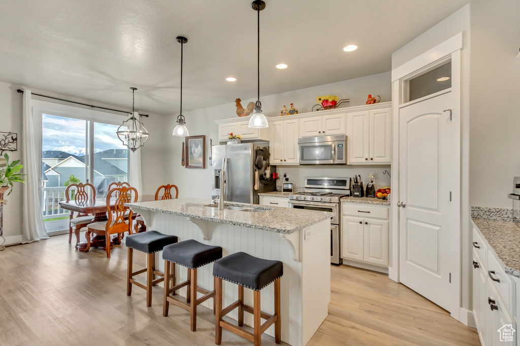 Kitchen featuring appliances with stainless steel finishes, light wood finished floors, a breakfast bar, white cabinetry, and a center island with sink