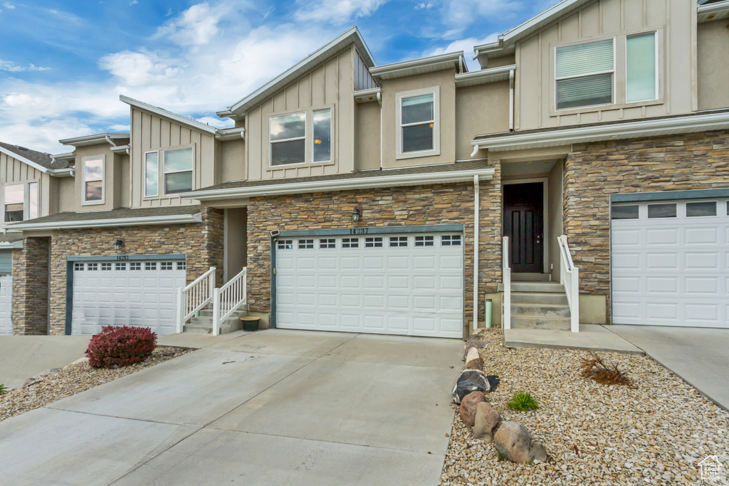 Multi unit property featuring board and batten siding, an attached garage, stone siding, and concrete driveway