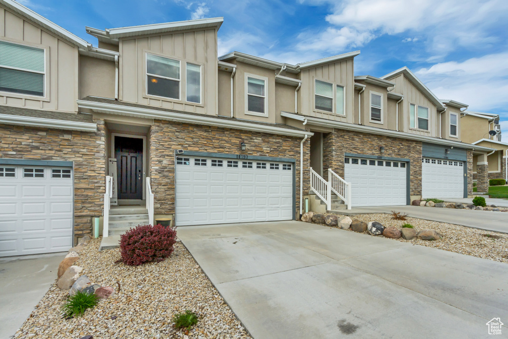 Townhome / multi-family property featuring board and batten siding, an attached garage, stone siding, and concrete driveway