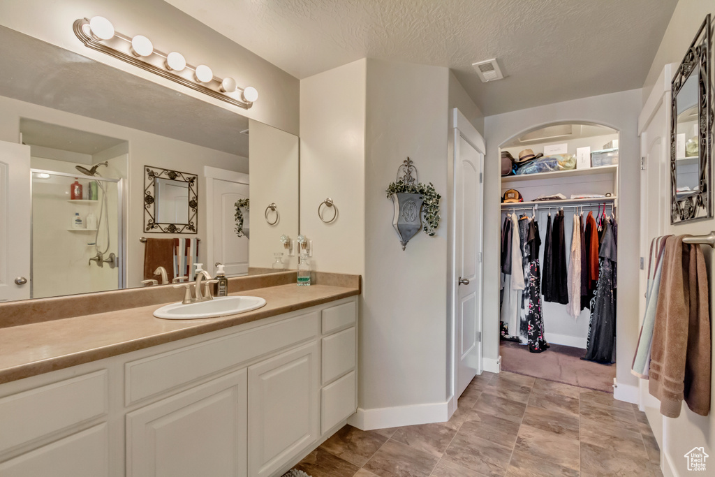 Bathroom featuring a shower stall, vanity, baseboards, a spacious closet, and a textured ceiling