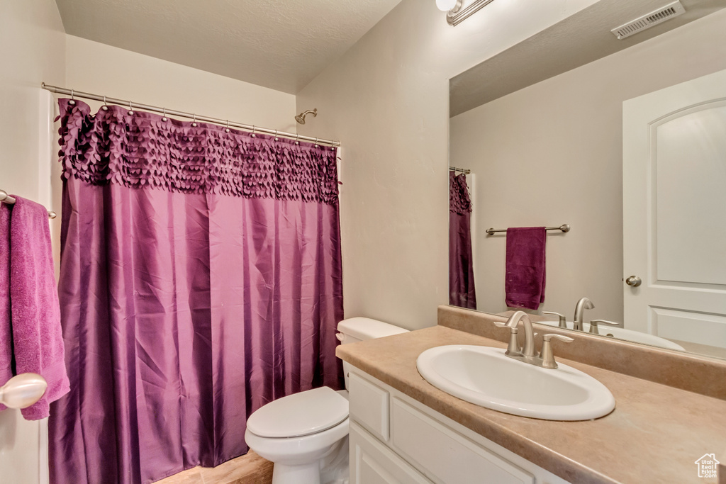 Bathroom with toilet, vanity, and curtained shower