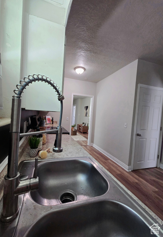 Kitchen view of wood finished floors, a textured ceiling, baseboards, and a sink