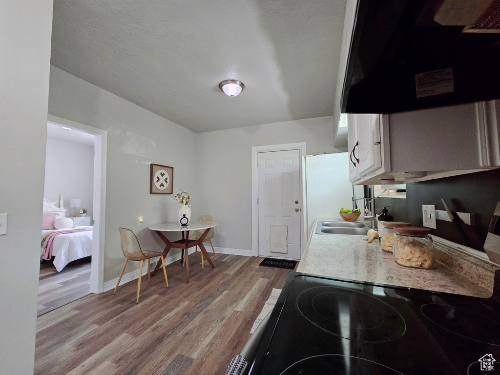 Kitchen with light countertops, light wood finished floors, ventilation hood, baseboards, and black range with electric stovetop