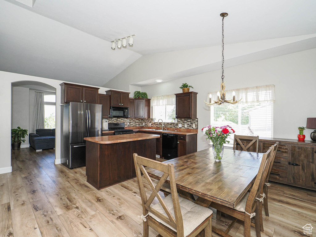 Dining space with vaulted ceiling, arched walkways, a chandelier, and light wood-style floors