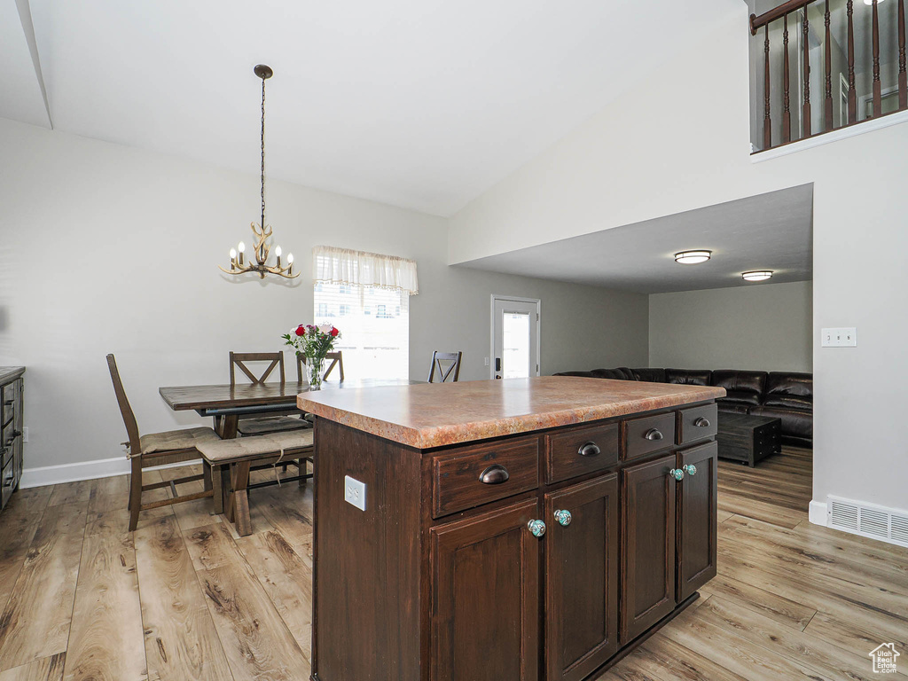 Kitchen featuring light wood finished floors, vaulted ceiling, dark brown cabinets, a chandelier, and pendant lighting