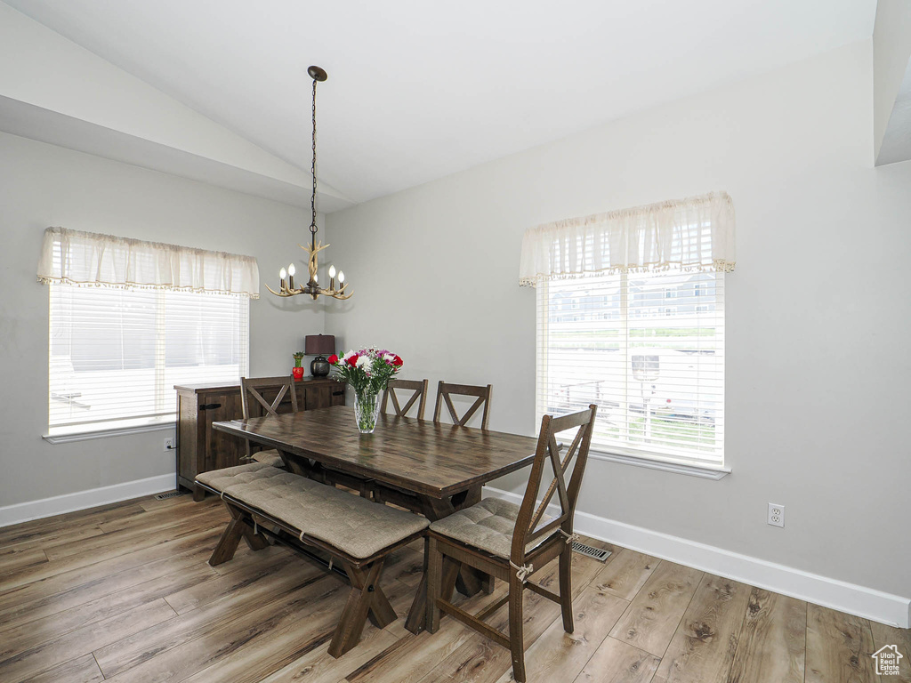 Dining space with a chandelier, light wood-style flooring, vaulted ceiling, and baseboards