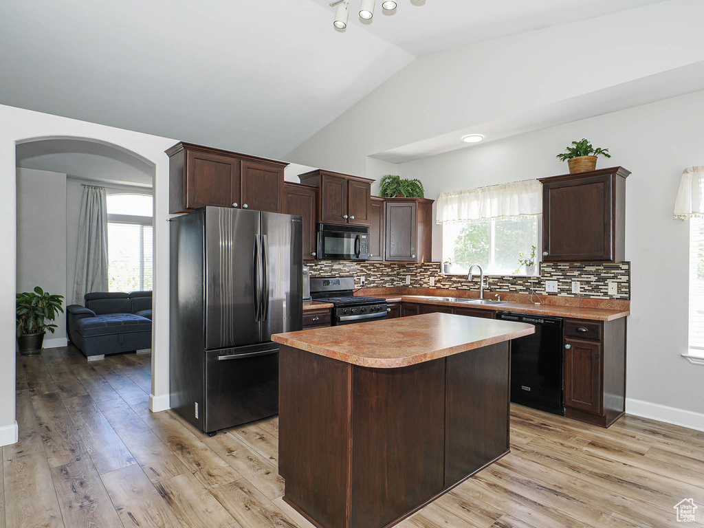 Kitchen with black appliances, a sink, arched walkways, dark brown cabinetry, and vaulted ceiling