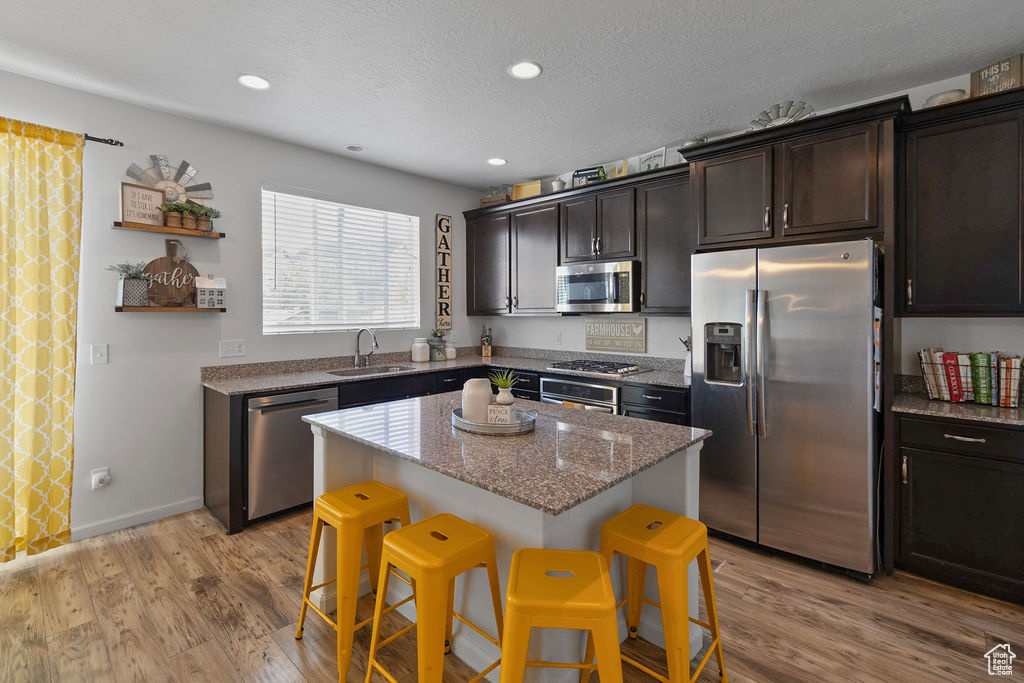 Kitchen with stainless steel appliances, a sink, a kitchen breakfast bar, a kitchen island, and light wood-style flooring