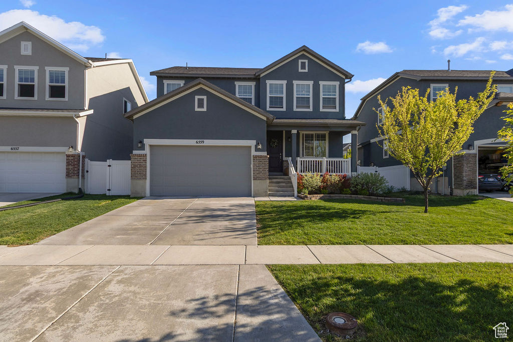 View of front of home with covered porch, stucco siding, brick siding, driveway, and a gate