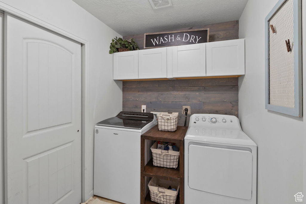 Clothes washing area with cabinet space, washing machine and dryer, and a textured ceiling