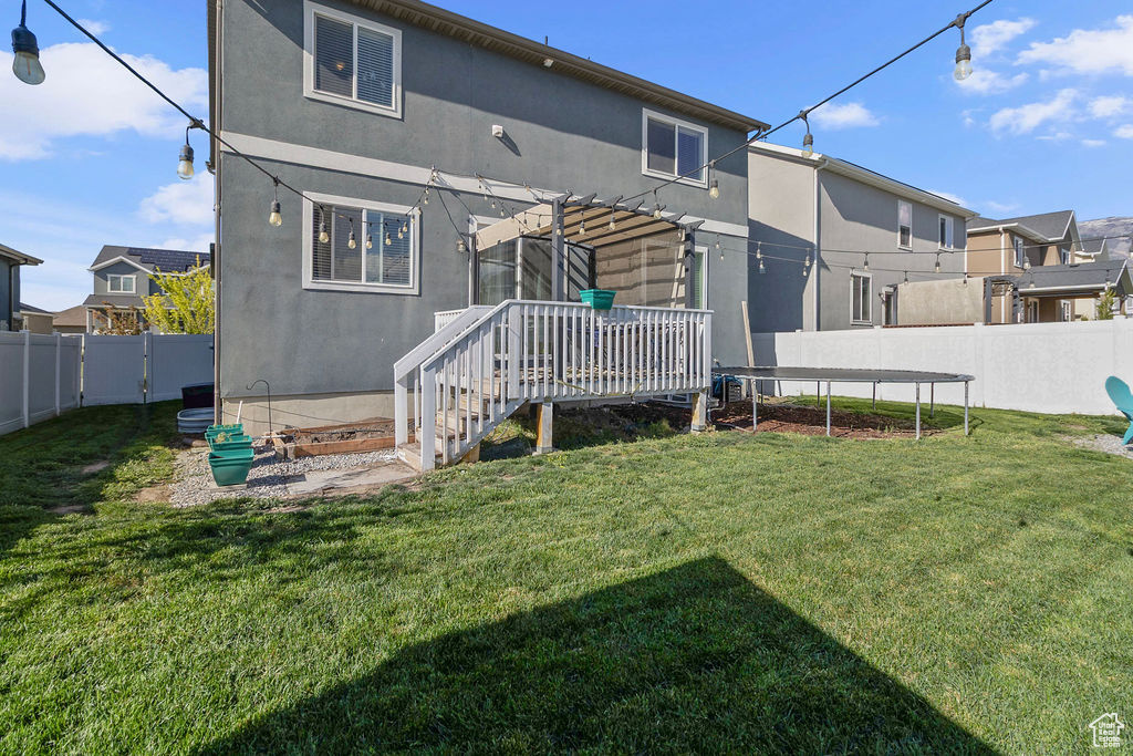 Back of property with a trampoline, stucco siding, a pergola, and a wooden deck