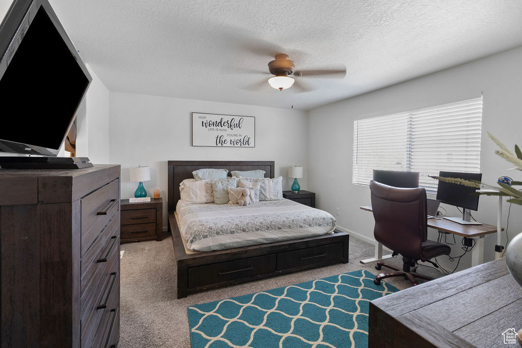 Carpeted bedroom featuring a textured ceiling, a desk, and a ceiling fan