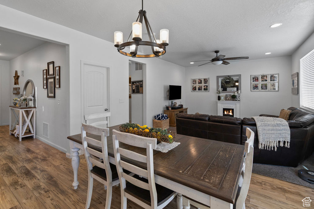 Dining space featuring ceiling fan, a chandelier, wood finished floors, recessed lighting, and a lit fireplace
