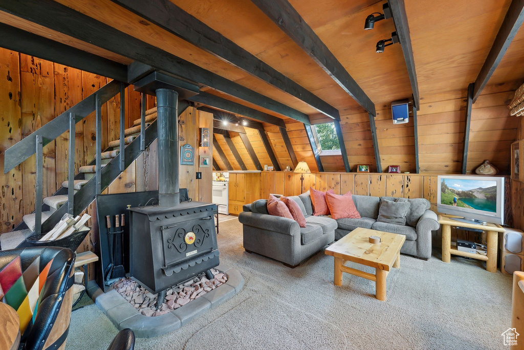 Living room featuring wood walls, a wood stove, carpet floors, and beam ceiling