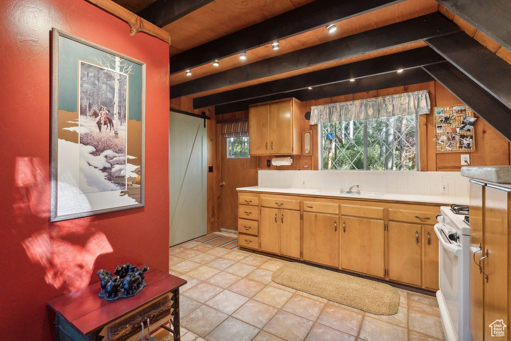Kitchen with light countertops, white gas stove, beamed ceiling, a sink, and wood walls