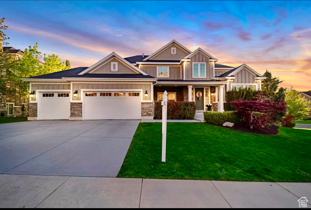 View of front of house with board and batten siding, a garage, concrete driveway, a front lawn, and stone siding