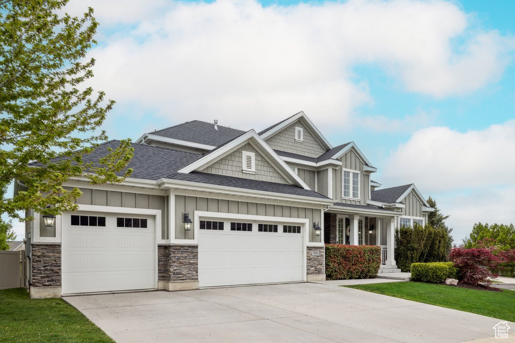 Craftsman-style home featuring board and batten siding, roof with shingles, driveway, a garage, and stone siding