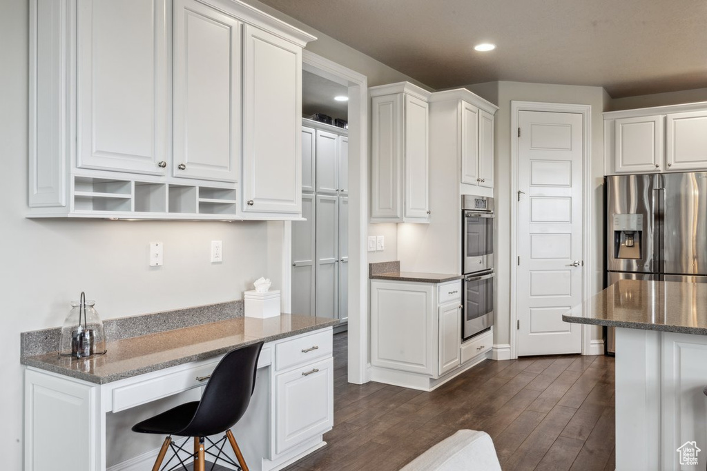 Kitchen with appliances with stainless steel finishes, white cabinets, recessed lighting, dark wood-style floors, and a breakfast bar area